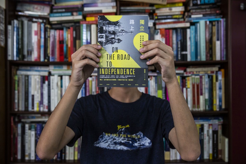 This picture taken on August 8, 2020 shows teenager Tony Chung holding up a copy of a book that police seized as evidence from his home when he was arrested under the new national security law, at a bookstore in Hong Kong. - Chung said he was walking through a shopping mall when police officers from Hong Kong's new national security unit swooped, bundled him into a nearby stairwell and scanned his face to unlock his phone. Chung's alleged crime was to write comments on social media that endangered national security, one of four students -- including a 16-year-old girl -- detained for the same offence that day. (Photo by ISAAC LAWRENCE / AFP) / TO GO WITH HongKong-China-politics,FOCUS by Su Xinqi and Jerome Taylor