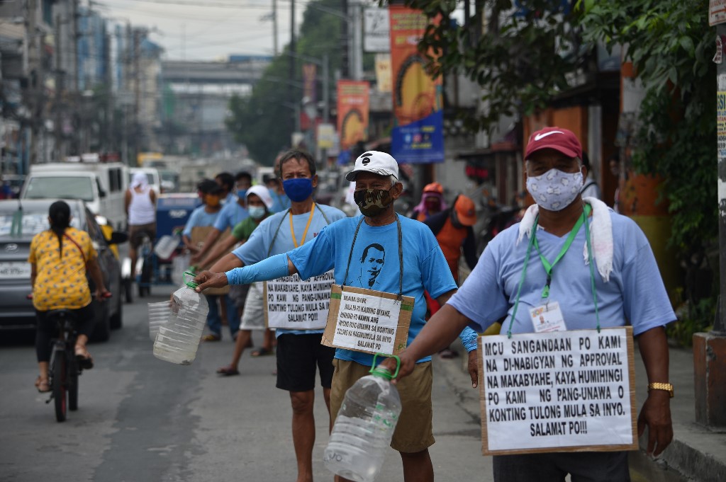 In this photo taken on August 12, 2020, a group of jeepney drivers with placards strapped along their bodies with writings "Mam/sir, we're jeepney drivers, asking for your help", beg for alms along a road in Manila. - Jeepney drivers have not picked up passengers in Manila since March when the popular minibuses were forced off the road by a coronavirus lockdown that has left millions out of work. (Photo by Ted ALJIBE / AFP) / TO GO WITH AFP STORY: Health-virus-Philippines-transport, FOCUS by Ron LOPEZ