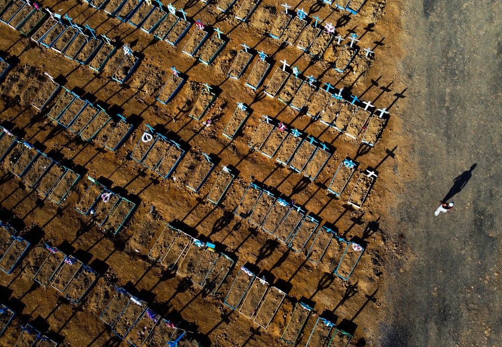 (FILES) This file photo taken on June 21, 2020 shows an aerial view of a man walking past graves in the Nossa Senhora Aparecida cemetery in Manaus on June 21, 2020. - Just over six months after registering its first case of the new coronavirus, Brazil -a country of 212 million people- has now registered 120,262 deaths from the virus and 3,846,153 infections, the health ministry said in its daily update. (Photo by MICHAEL DANTAS / AFP)