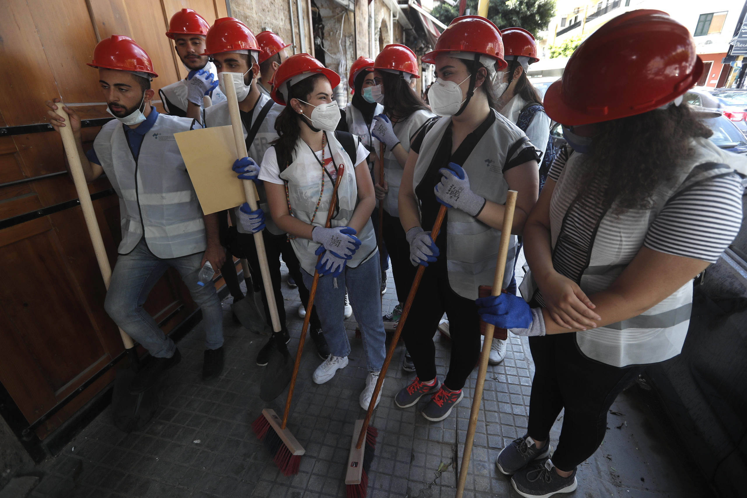 People who volunteered to help clean damaged homes and give other assistance, gather on a street that was damaged by last week's explosion, in Beirut, Lebanon, Tuesday, Aug. 11, 2020. The explosion that tore through Beirut left around a quarter of a million people with homes unfit to live in. In the absence of the state, residents of Beirut opened their homes to relatives, friends and neighbors. And on the streets, it was young volunteers with brooms and shovels, not government workers, who cleared the littered streets. (AP Photo/Hussein Malla)