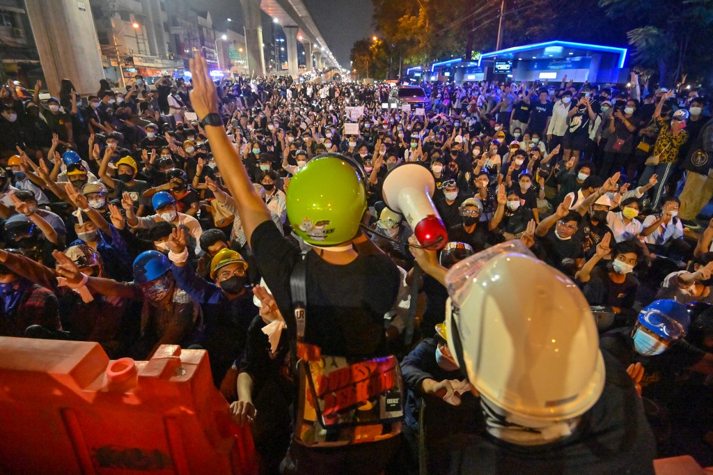 A pro-democracy protester uses a loudspeaker to talk to the crowd and gives the three-finger salute during an anti-government rally at Kaset intersection in Bangkok on October 19, 2020, as they continue to defy an emergency decree banning gatherings. (Photo by Mladen ANTONOV / AFP)