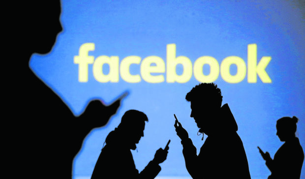Silhouettes of mobile users are seen next to a screen projection of the Facebook logo in this picture illustration taken March 28, 2018.