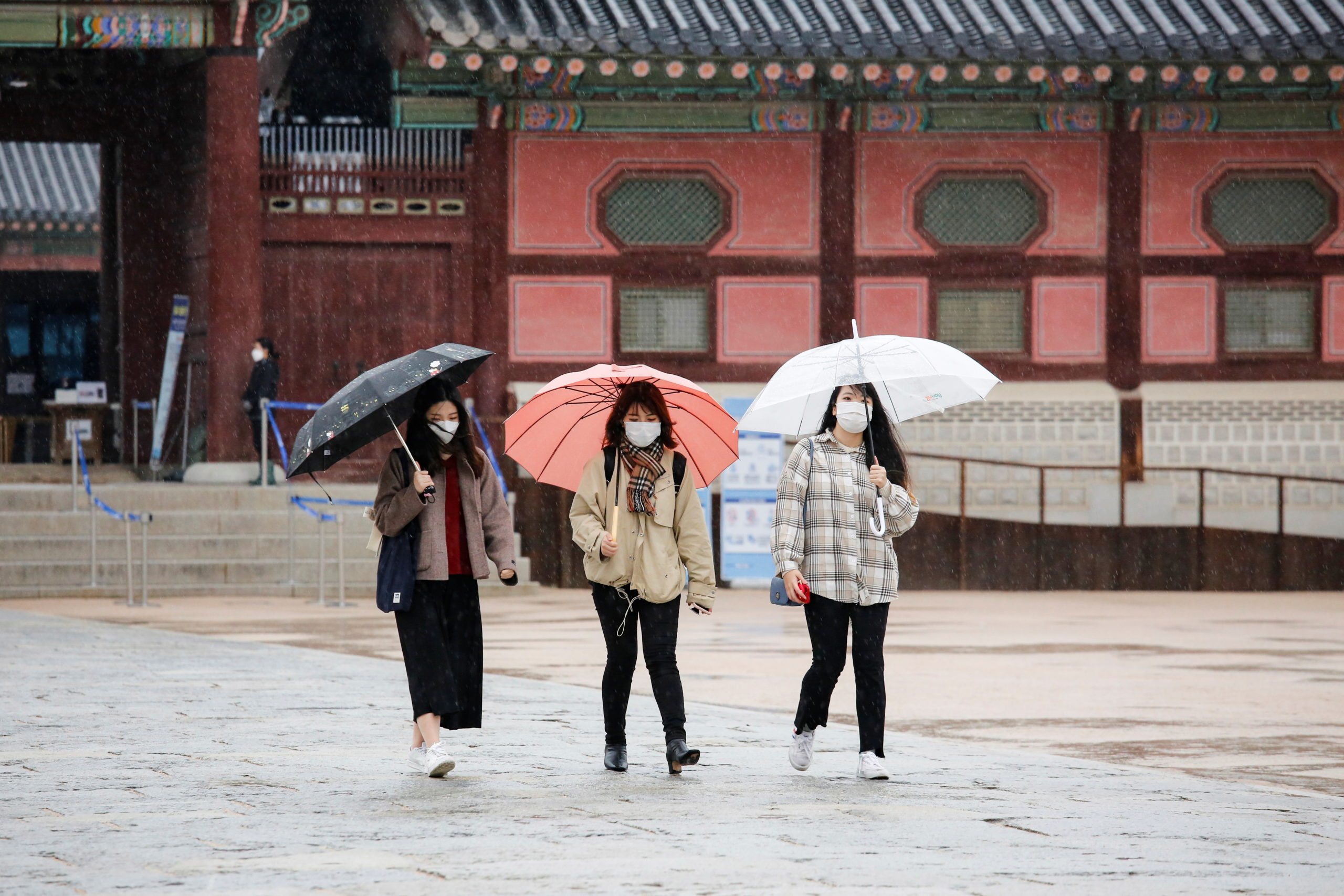 Tourists wearing masks walk with umbrellas as it rains amid the coronavirus disease (COVID-19) pandemic at Gyeongbok Palace in central Seoul, South Korea, November 19, 2020.    REUTERS/Heo Ran