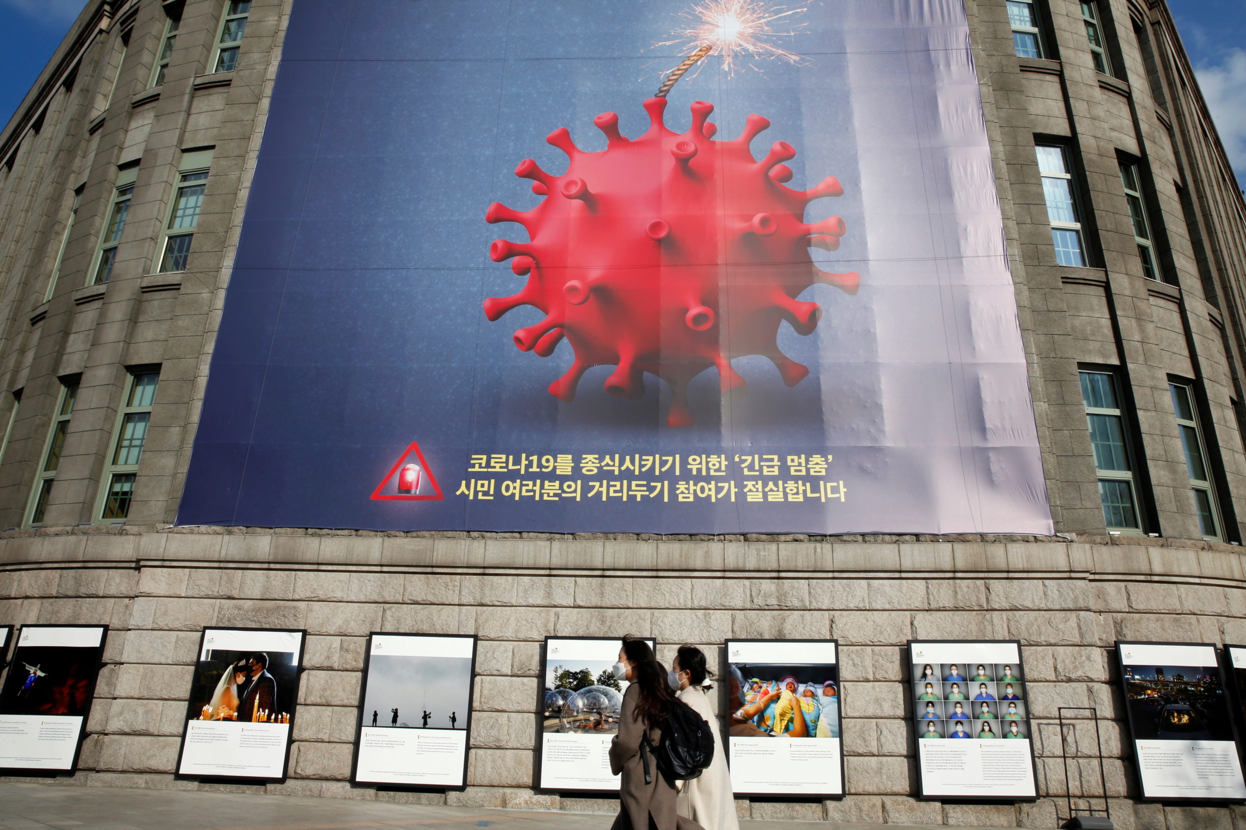 FILE PHOTO:  Women wearing face masks walk past a banner promoting a social distancing campaign displayed on the wall of Seoul City Hall in Seoul, South Korea, November 27, 2020.   REUTERS/Heo Ran/File photo