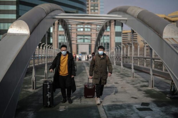 men wearing face masks with luggage in tow