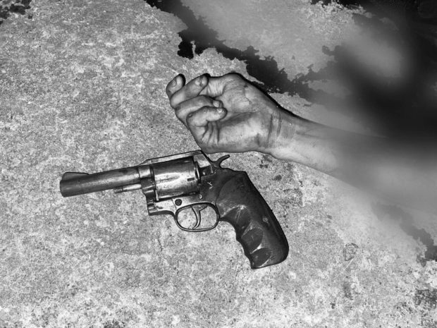 Police show a firearm near the bloody hand of one of the suspected robbers, who were killed in a police chase along Barangay Pasong Tamo.