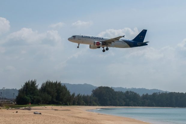 This photo taken on January 30, 2021 shows a Thai AirAsia Airbus A320 passenger airplane flying over an empty beach as it lands at Phuket International Airport in Phuket. (Photo by Alex OGLE / AFP)