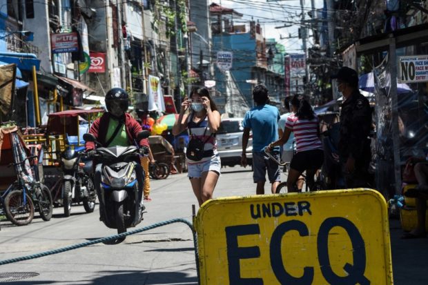 A policeman (R) monitors people at the entrance to a neighbourhood under strict quarantine measures in Pasay City, suburban Manila, on March 16, 2021, as the number of new daily cases of Covid-19 coronavirus has surged to the highest level in seven months.
