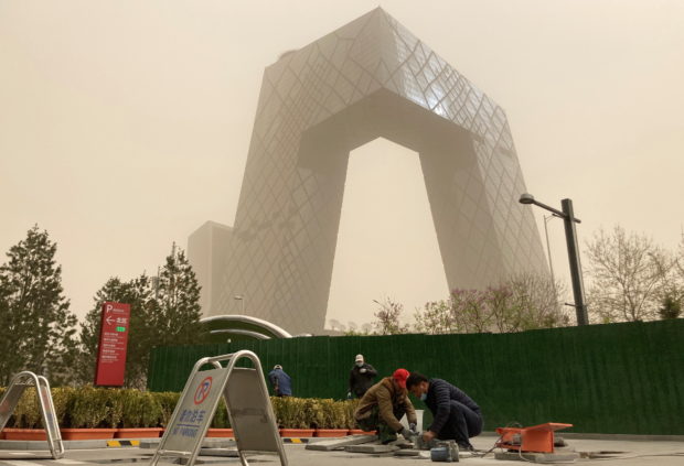 Construction workers are seen in front of the CCTV headquarters shrouded in dust as the city is hit by a sandstorm, in Beijing