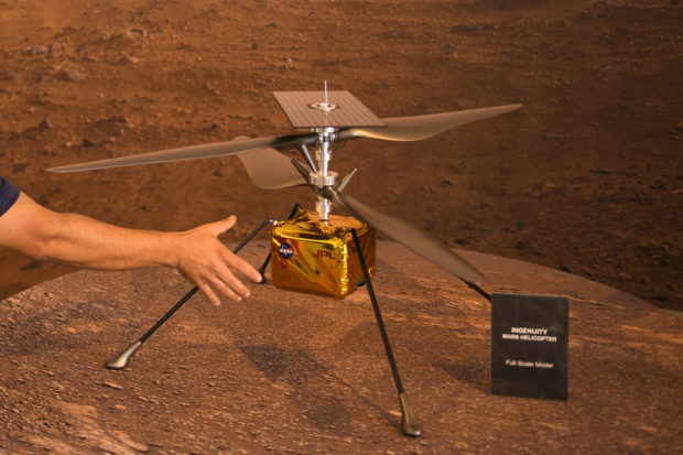 A staff member places a full-scale model of the Ingenuity Mars Helicopter at NASA's Jet Propulsion Laboratory (JPL) on a table ahead of the Mars 2020 Perseverance rover landing on February 18, 2021 in Pasadena, California. - The Mars exploration rover will search for signs of ancient microbial life and collect rock samples for future return to Earth to study the red planet's geology and climate, paving the way for human exploration. Perseverance also carries the experimental Ingenuity Mars Helicopter - which will attempt the first powered, controlled flight on another planet. (Photo by Patrick T. FALLON / AFP)