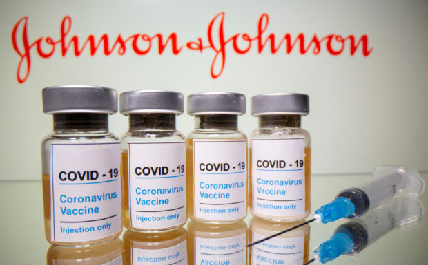 Vials with a sticker reading, "COVID-19 / Coronavirus vaccine / Injection only" and a medical syringe are seen in front of a displayed Johnson & Johnson logo in this illustration taken October 31, 2020