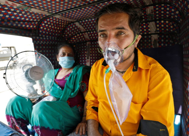 A patient wearing an oxygen mask looks on as his wife holds a battery-operated fan while waiting inside an auto-rickshaw to enter a COVID-19 hospital for treatment, amidst the spread of the coronavirus disease (COVID-19) in Ahmedabad, India, April 25, 2021. REUTERS/Amit Dave