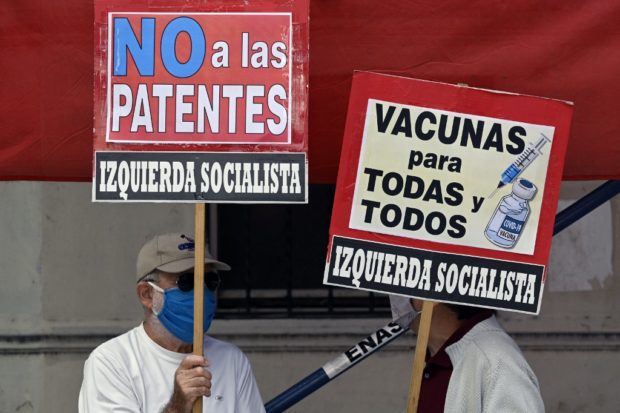 People hold banners reading “Vaccines for all” and “No to patents” during a protest of members of leftist parties outside the World Health Organization (WHO) headquarters in Buenos Aires, on April 14, 2021, amid the coronavirus pandemic. (Photo by JUAN MABROMATA / AFP)