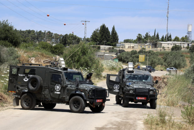 Jeeps belonging to Israeli security forces used as a barrier near the Salem checkpoint on a road leading to the West Bank town of Jenin, following an attack by Palestinians on an Israeli base, pictured in the background, on May 7, 2021. - Two Palestinians were killed and a third critically wounded today after they opened fire on an Israeli base in the occupied West Bank, the Israeli border police said. The attack near the northern West Bank town of Jenin was the second shooting in the territory this week, and came as tensions soar in annexed east Jerusalem over an eviction threat hanging over four Palestinian families.