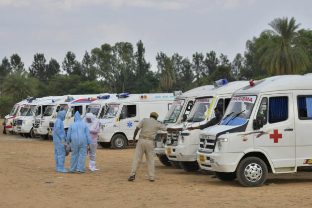Family members and relatives wearing protective gear stand next to ambulances carrying the bodies of victims who died of the Covid-19 coronavirus at an open air crematorium set up for the coronavirus victims inside a defunct granite quarry on the outskirts of Bangalore on May 8, 2021, as India recorded more than 4,000 coronavirus deaths in a day for the first time. - Family members and relatives wearing protective gear stand next to ambulances carrying the bodies of victims who died of the Covid-19 coronavirus (Photo by Manjunath Kiran / AFP)