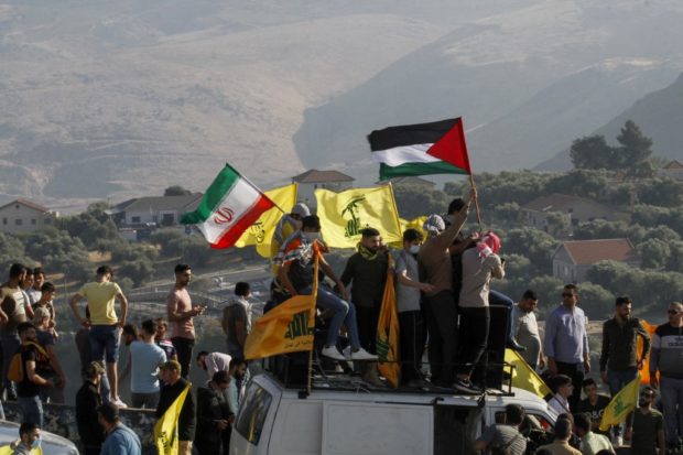 In this file photo taken on May 14, 2021 Supporters of Lebanon's Hezbollah lift its flags (C) alongside those of Iran (L) and Palestine, during an anti-Israel protest in the southern Khiam area by the border with Israel, facing the northern Israeli town of Metula. - Israel's deadly Gaza offensive has many eyes trained on the Lebanese border for a Hezbollah reaction but observers argue the Iran-backed movement is unlikely to risk an all-out conflict. Hezbollah and the Palestinian Hamas, both designated as terrorist groups by Israel and much of the West, have mended fences after ending up on opposing sides of the Syrian war a decade ago
