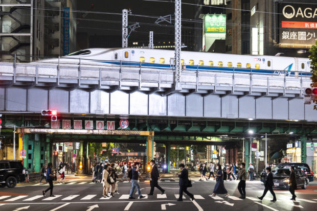 People cross a street as a shinkansen, or high speed bullet train, arrives in Tokyo on May 19, 2021. (Photo by Charly TRIBALLEAU / AFP)