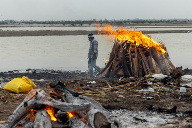 A man walks past burning pyres with people who died from the coronavirus disease (COVID-19), on the banks of the river Ganges at Garhmukteshwar in the northern state of Uttar Pradesh, India, May 6, 2021. REUTERS/Danish Siddiqui