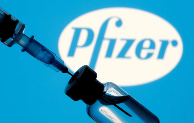 Vial and sryinge are seen in front of displayed Pfizer logo