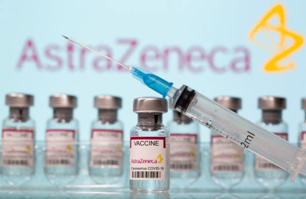 Vials labelled "AstraZeneca COVID-19 Coronavirus Vaccine" and a syringe are seen in front of a displayed AstraZeneca logo in this illustration taken March 10, 2021