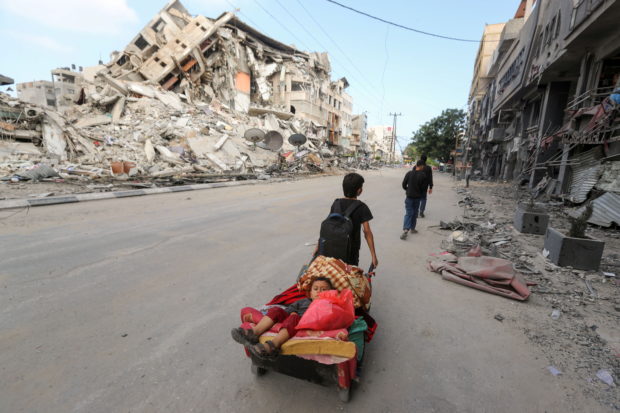 A Palestinian boy pulls a cart carrying his brother and their belongings as they flee their home during Israeli air and artillery strikes, near the site of a tower building destroyed in earlier strikes in Gaza City May 14, 2021