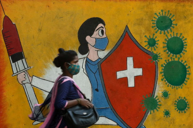 A woman walks past a graffiti on a street, amidst the spread of the coronavirus disease (COVID-19) in Mumbai, India, May 10, 2021