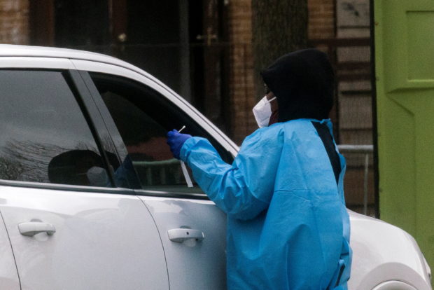 A health worker does a coronavirus disease (COVID-19) test as people wait at a drive-through COVID-19 testing center in a local street, in Newark, New Jersey