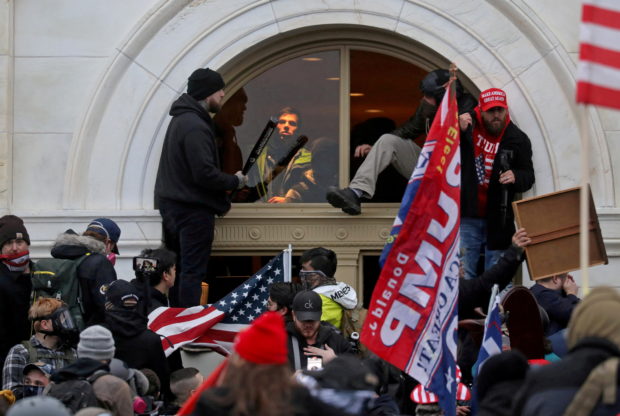 A mob of supporters of then-U.S. President Donald Trump climb through a window they broke as they storm the U.S. Capitol Building in Washington, U.S., January 6, 2021. REUTERS/Leah Millis
