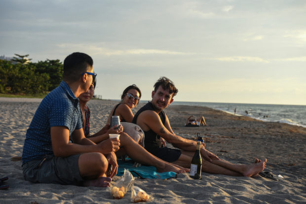 This photo taken on June 2, 2021 shows digital nomad, Carlo Almendral (L), the chief executive of an artificial intelligence start-up, sitting with others as they relax at the beach in the town of San Juan, La Union province, north of Manila. - Many digital workers in congested Manila, fearing Covid-19 and fed up with lockdowns and restrictions, are escaping to largely deserted nature hotspots to do their jobs -- injecting much-needed money into communities dependent on outside visitors. (Photo by Maria TAN / AFP) / TO GO WITH AFP STORY PHILIPPINES-HEALTH-VIRUS-LEISURE-ECONOMY, FOCUS BY ALLISON JACKSON / The erroneous mention[s] appearing in the metadata of this photo by Maria TAN has been modified in AFP systems in the following manner: [name as Carlo Almendral, and caption info] instead of [Carlo Almendal]. Please immediately remove the erroneous mention[s] from all your online services and delete it (them) from your servers. If you have been authorized by AFP to distribute it (them) to third parties, please ensure that the same actions are carried out by them. Failure to promptly comply with these instructions will entail liability on your part for any continued or post notification usage. Therefore we thank you very much for all your attention and prompt action. We are sorry for the inconvenience this notification may cause and remain at your disposal for any further information you may require.