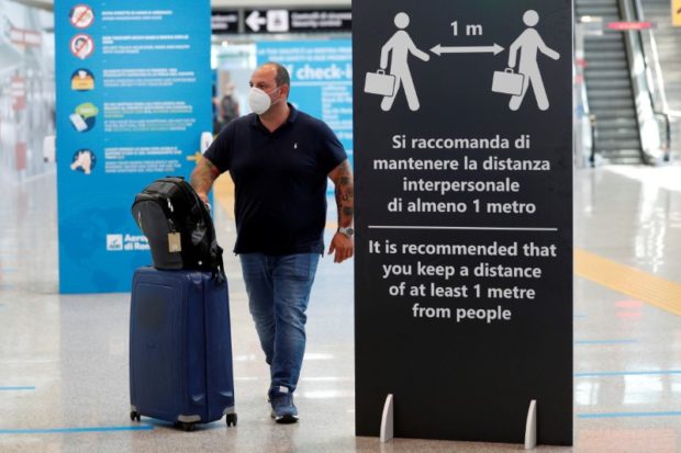 A passenger wearing a protective face mask walks past a sign indicating to keep the social distancing at Fiumicino Airport, one of the two airports in the world to obtain the 'Biosafety Trust certification' for the correct application of security measures to prevent infections, following the coronavirus disease (COVID-19) outbreak, in Rome, Italy June 30, 2020. 