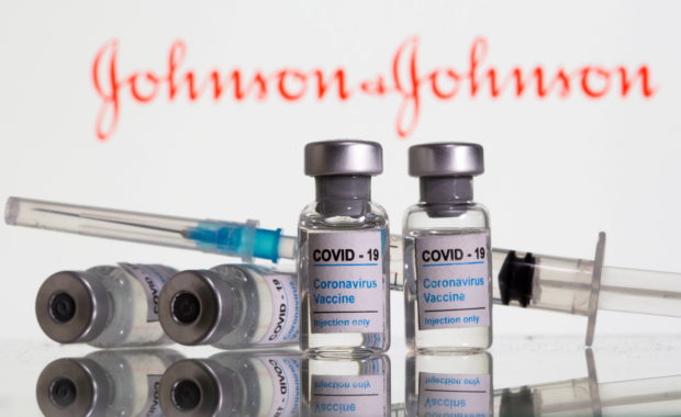  Vials labeled "COVID-19 Coronavirus Vaccine" and syringe are seen in front of displayed J&J logo in this illustration