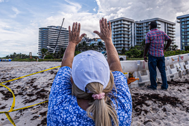 A woman prays as rescue workers search the rubble at the site of the partially collapsed 12-story Champlain Towers South condo building in Surfside, Florida, on July 2, 2021. - Two more victims were found in the rubble of a collapsed apartment building in Florida, including the body of a seven-year-old girl, bringing the death toll from last week's tragedy to 20, with 128 people still unaccounted for, officials said on July 2, 2021. (Photo by Giorgio Viera / AFP)