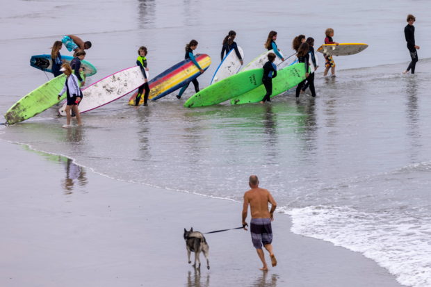  A man runs with his dog as a surfing class enters the ocean during a heatwave in Oceanside, California, U.S., June 17, 2021.  A man runs with his dog as a surfing class enters the ocean during a heatwave in Oceanside, California, U.S., June 17, 2021. 