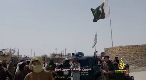 People stand in front of a vehicle as an Islamic Emirate of Afghanistan and a Pakistan's flag flutter in front of the friendship gate of Afghanistan and Pakistan at the Wesh-Chaman border crossing, Spin Boldak, Afghanistan July 14, 2021, in this screen grab obtained from a video. 