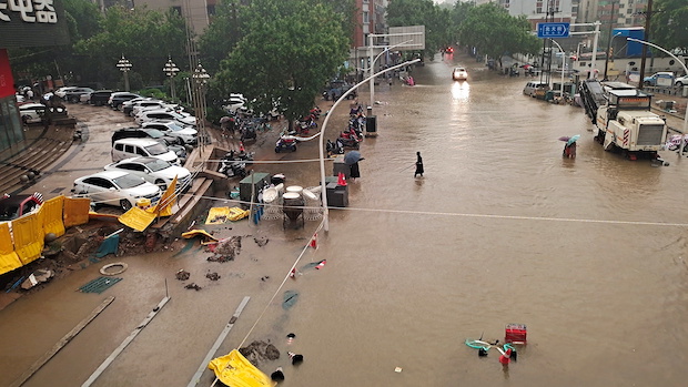 People wade through floodwaters on a road amid heavy rainfall in Zhengzhou
