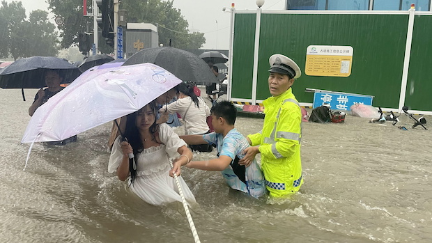 Traffic police officer guides residents to cross a flooded road with a rope during heavy rainfall in Zhengzhou