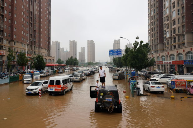 Men stand on a vehicle on a flooded road following heavy rainfall in Zhengzhou, Henan province, China July 23, 2021. 