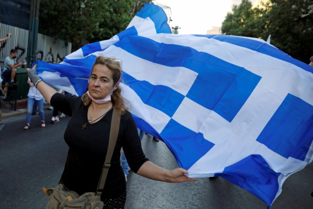 An anti-vaccine demonstrator holds a Greek flag during a protest against coronavirus disease (COVID-19) vaccinations, in Athens, Greece, July 24, 2021.