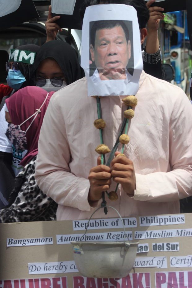 A pot and a garland of raw camote (sweet potato) are hung on a man who impersonates President Duterte, to symbolize an 'award of failure' to his administration