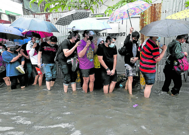 ADDED RISK Residents and workers stand in the rain and wade through floodwaters on Wednesday—risking infection from waterborne diseases—just to get into San Andres Sports Complex in Manila, one of the COVID-19 vaccination hubs in the city. —RICHARD A. REYES