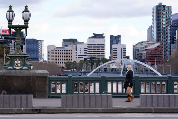 A lone woman, wearing a protective face mask, walks across an unusually quiet city centre bridge on the first day of a lockdown as the state of Victoria looks to curb the spread of a coronavirus disease (COVID-19) outbreak in Melbourne, Australia, 