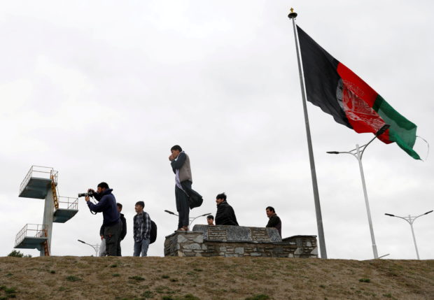 Youths take pictures next to an Afghan flag on a hilltop overlooking Kabul, Afghanistan,