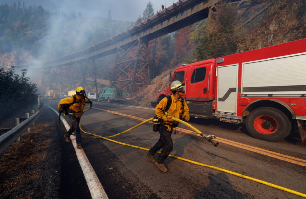 Firefighters run towards a spot fire while protecting a rail bridge from the Dixie Fire, a wildfire near the town of Quincy, California