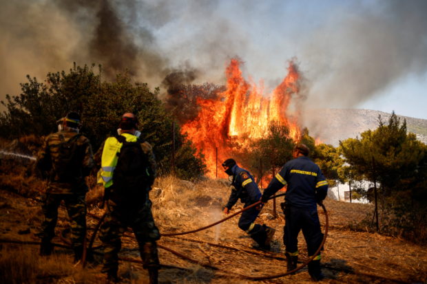 Firefighters and volunteers try to extinguish a wildfire burning in the village of Markati, near Athens, Greece, 