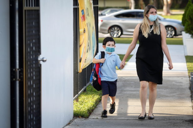 A teacher walks with a student, as they wear protective masks on the first day of school, amid the coronavirus disease (COVID-19) pandemic, at St. Lawrence Catholic School in North Miami Beach, Florida, U.S. August 18, 2021. REUTERS/Marco Bello