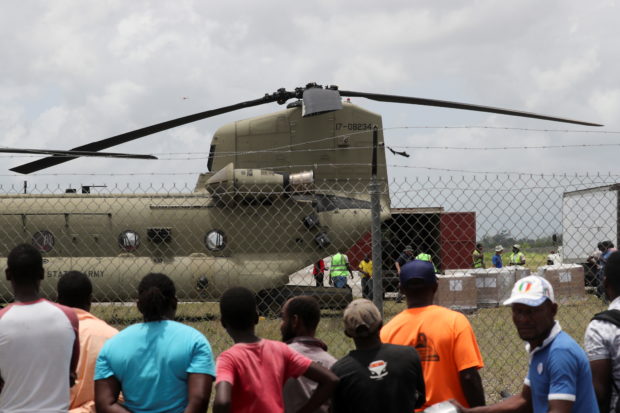 Residents look on as workers receive humanitarian aid from a U.S. helicopter at Les Cayes airport after Saturday's 7.2 magnitude earthquake, in Les Cayes, Haiti, August 18, 2021. REUTERS/Henry Romero