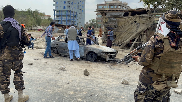 Afghan men take pictures of a vehicle from which rockets were fired, as Taliban forces stand guard, in Kabul