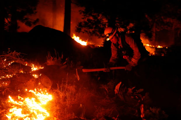 Austin Rhodes, 20, a fire fighter with the Fallen Leaf Lake Fire Department, works a hand line behind houses along Santa Clause Drive as flames from the Caldor Fire burn through trees in Christmas Valley near South Lake Tahoe, California, U.S., August 30, 2021.  