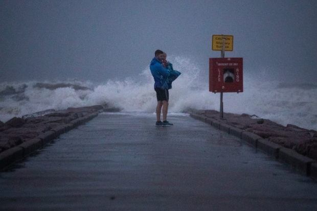 Local resident John Smith holds his 18-month-old son Owen as he stands near breaking waves on a pier ahead of the arrival of Tropical Storm Nicholas in Galveston, Texas, U.S., September 13, 2021. 