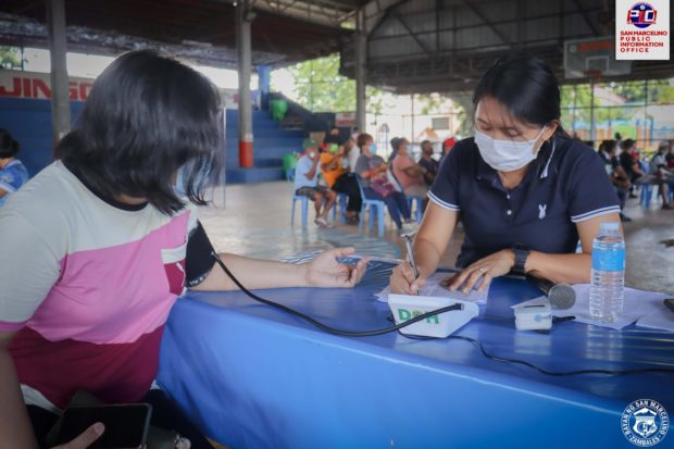 A health worker in Zambales province monitors a resident before administering a vaccine against COVID-19